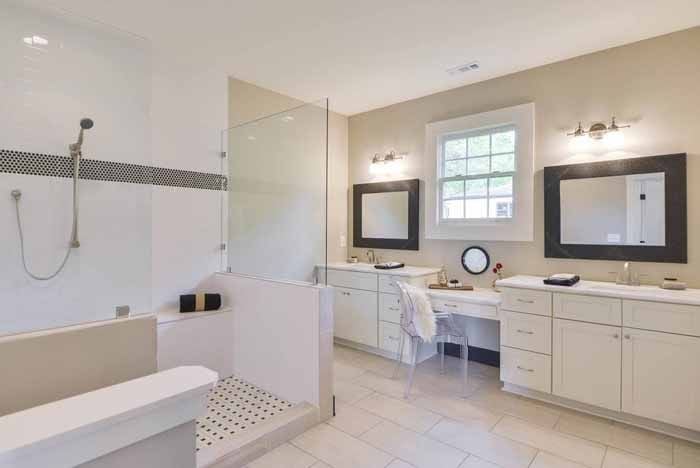 Bright bathroom with a glass shower, white vanities and dark framed mirrors