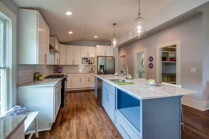 Blue kitchen island with light stone counters and white cabinetry