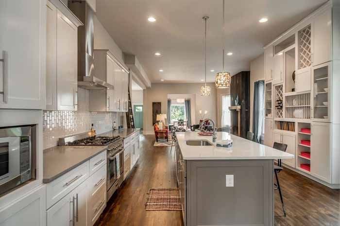 White kitchen with a long island, pendant lighting and wood floors